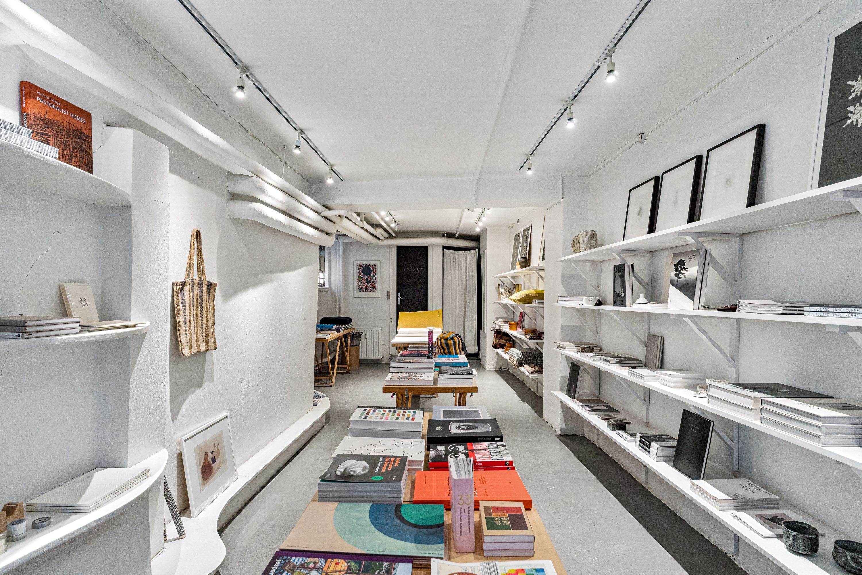 Boghandel med hylder fulde af bøger og design, store vinduer og en hyggeligt indrettet forside.