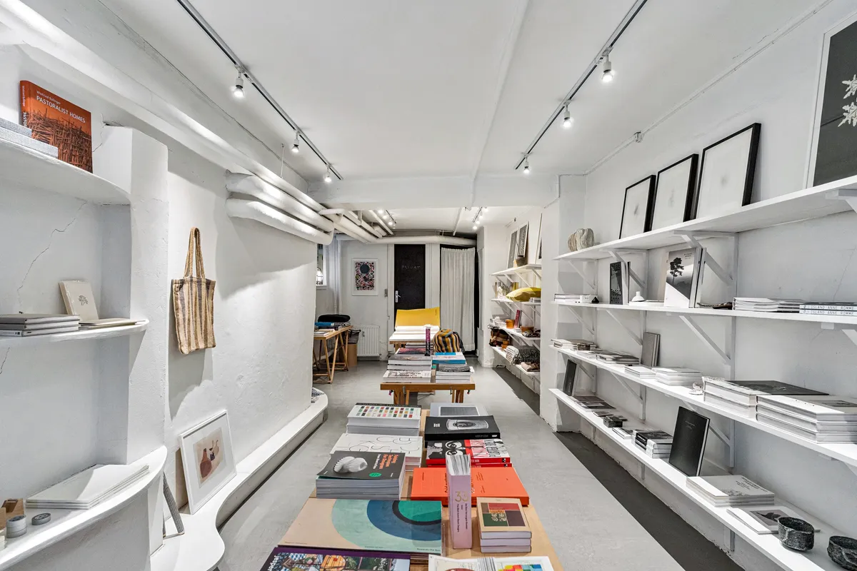 Boghandel med hylder fulde af bøger og design, store vinduer og en hyggeligt indrettet forside.