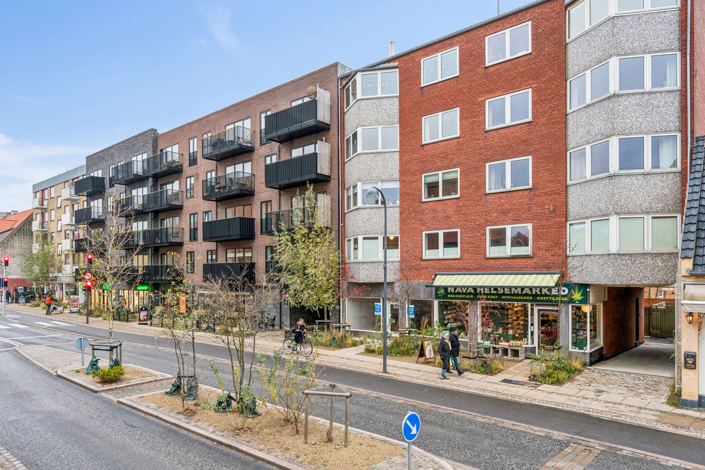 Butik til leje i Søborg med moderne bygninger, grønne planter og folk, der går forbi i forgrunden og baggrunden