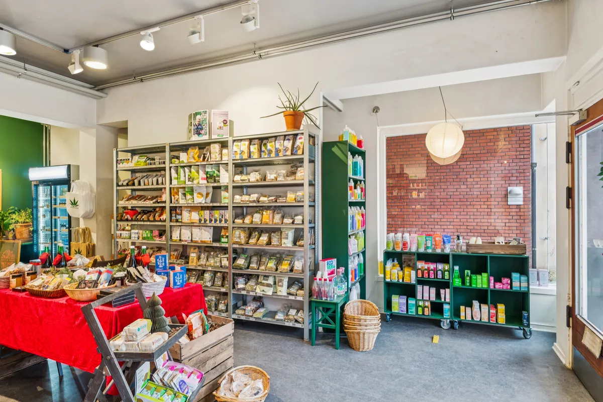 Inde i en smuk indretning af en butik er der flere hylder med produkter, en plante i jordbærpot og en lysekron med et hvidt kuppelformet lys