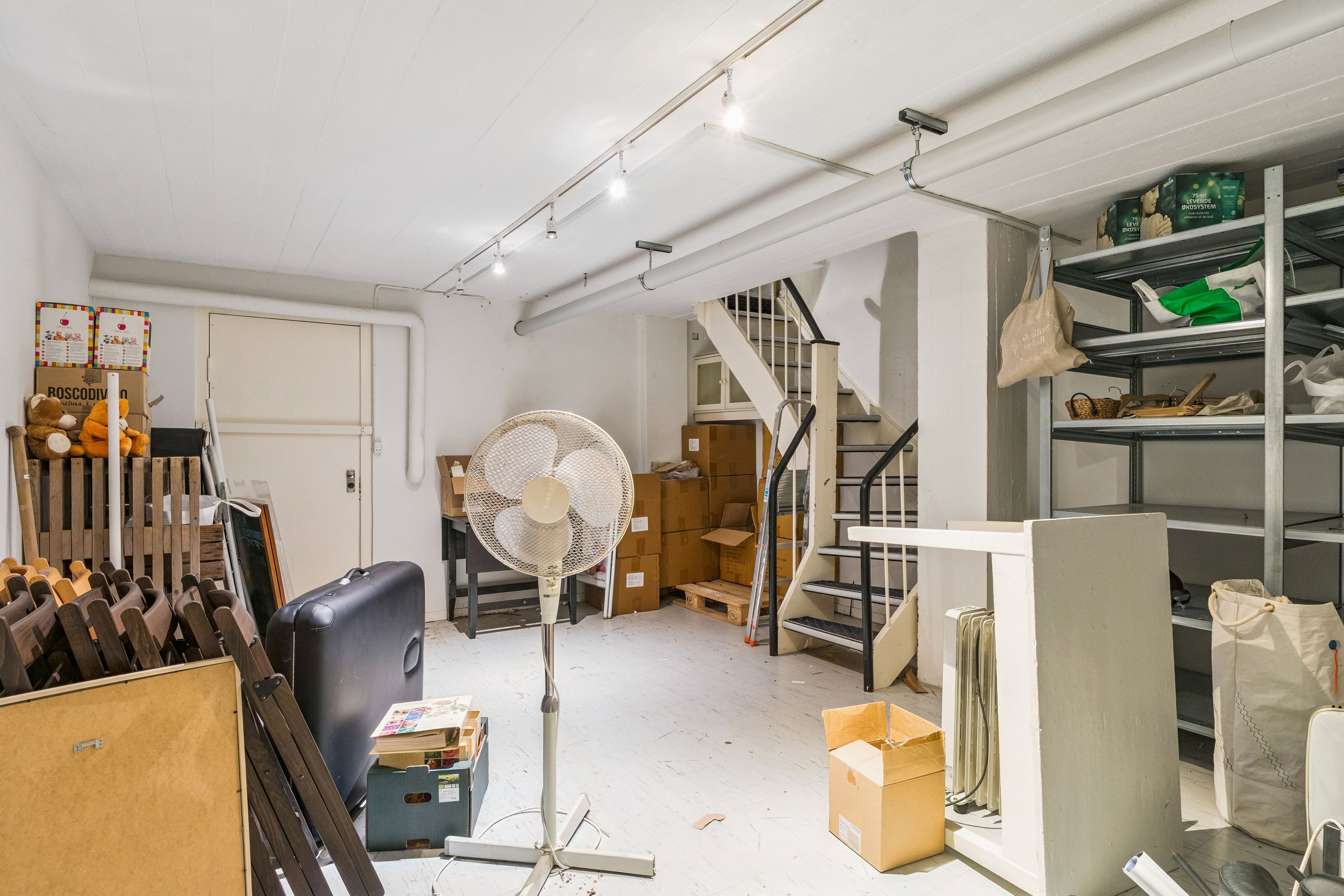 Butikslokale med lager og trappe til etage 2, 74 m² og 32 m² lager. Ledige lagerrum med vinduesfront og lagerhylder.