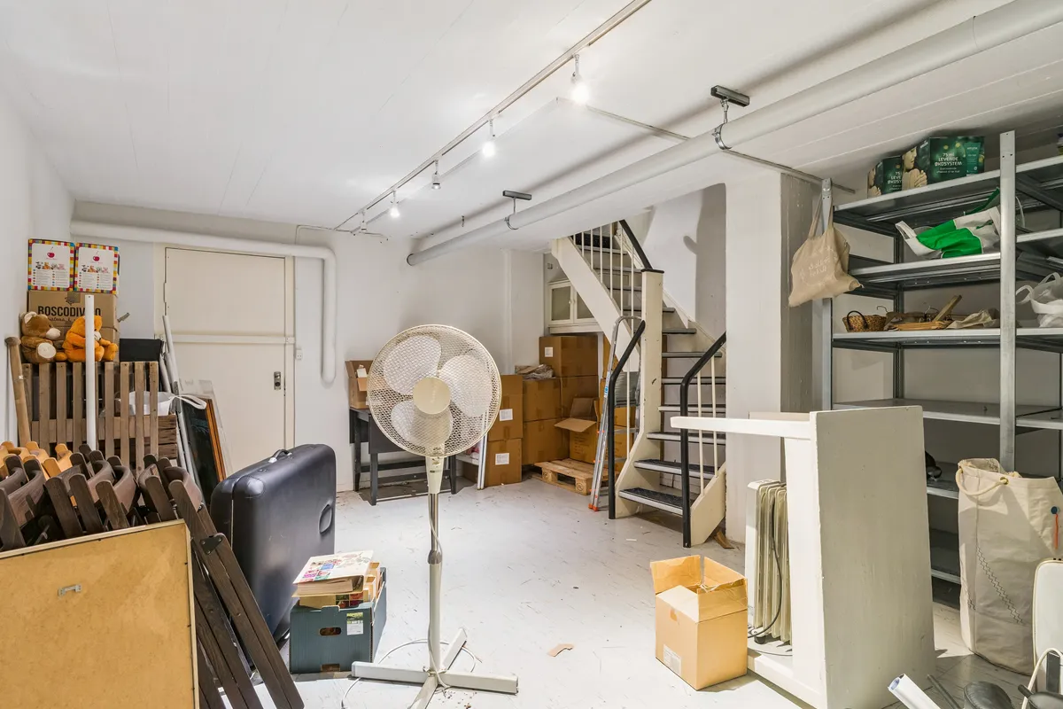 Butikslokale med lager og trappe til etage 2, 74 m² og 32 m² lager. Ledige lagerrum med vinduesfront og lagerhylder.