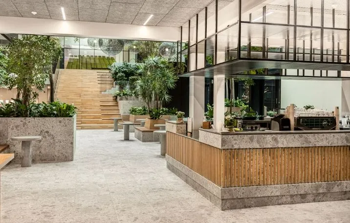 Naturligt lys trænger ind i lobbyen med marmorgulv og trætrapper, som fører op til et loft. Moderne møbler og planter placeret strategisk for at skabe en fredfyldt atmosfære.