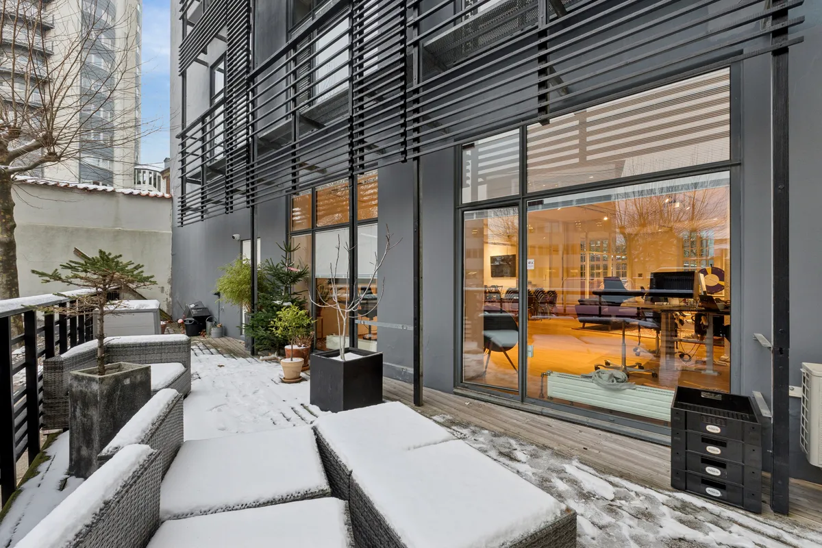 Moderne kontor med høj loftshøjde og privat terrasse med snedækket og plantepoteter, udsigt til en gul gulv og møbler samt udsigt til en høj bygning med store vinduer