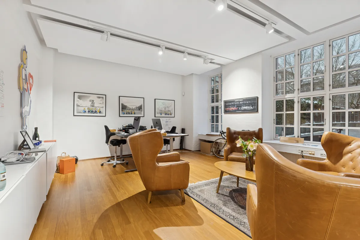 Kontorlokaler med lyse gulve, moderne møbler og flotte udsigtsvindue. Kontoret er udstyret med computere, skriveborde og smukke billeder på væggen.