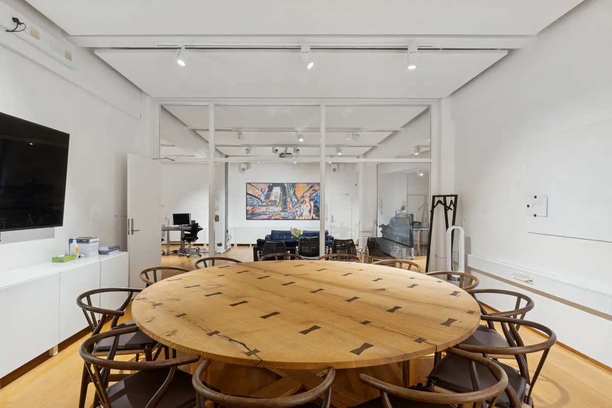 Lyst og moderne kontor med høj loftshøjde og privat terrasse på Vesterbrogade. Rundt træbord med stole i rummet og maleri på væggen.