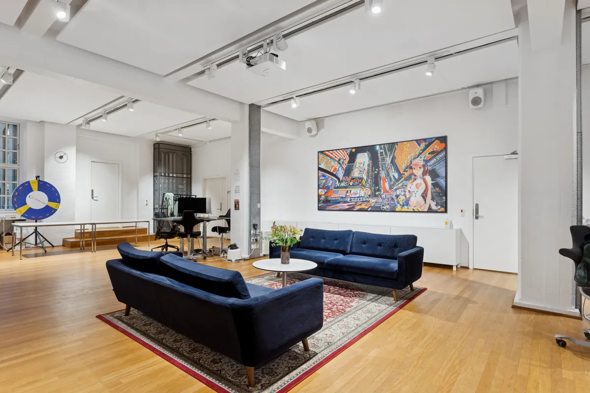 Moderne kontor med lyse lofter, højloftede værelser og terrasse. To blå sofaer med blomster i glas og et stort maleri. Lyse gulvbelægning og minimalistisk indretning.