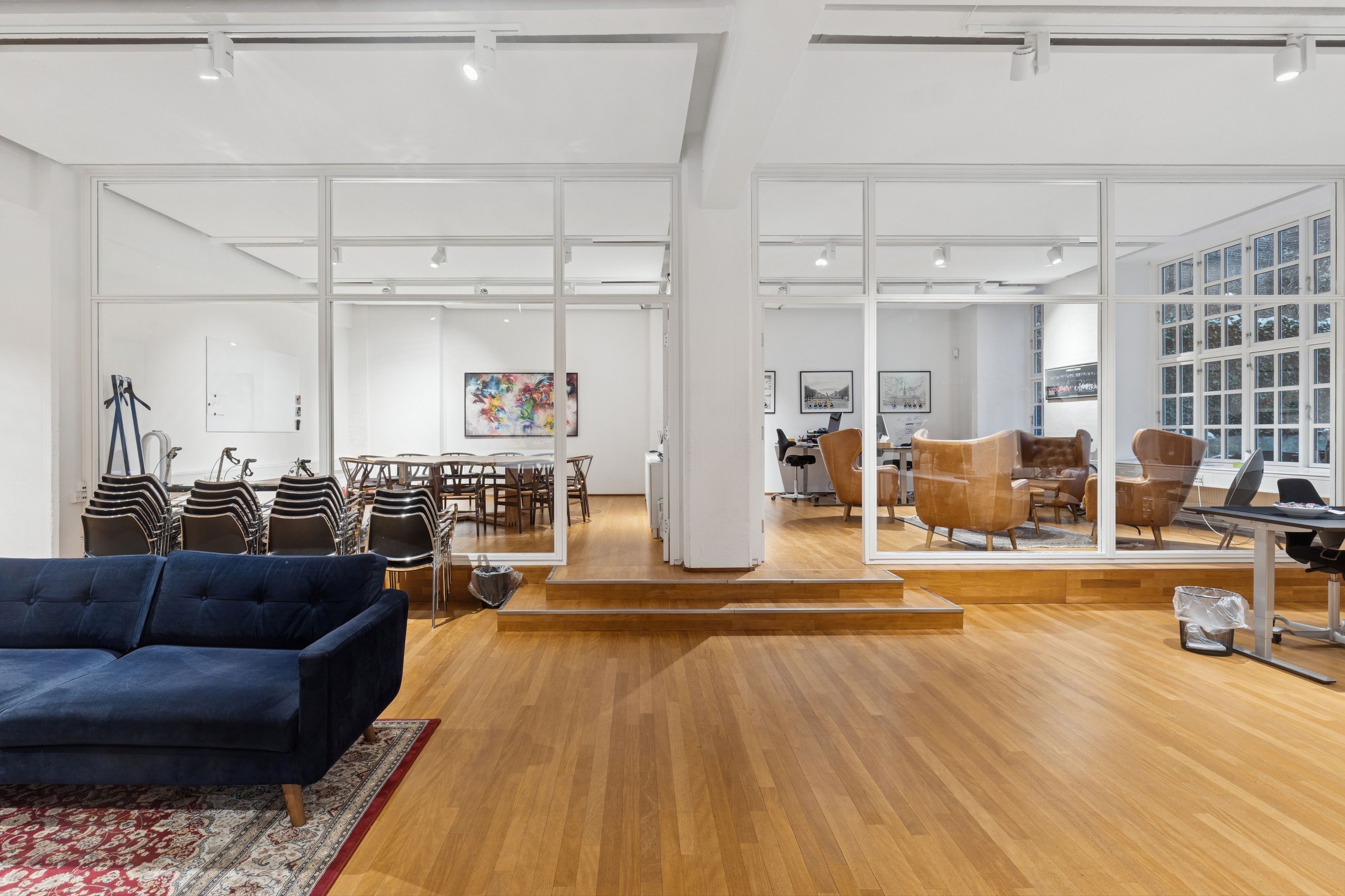 Lyst og moderne kontorrum med trægulv og møbler, fuld længde spejl og stolpe, lyse loftslys, terrasse og spisestue med borde og stole