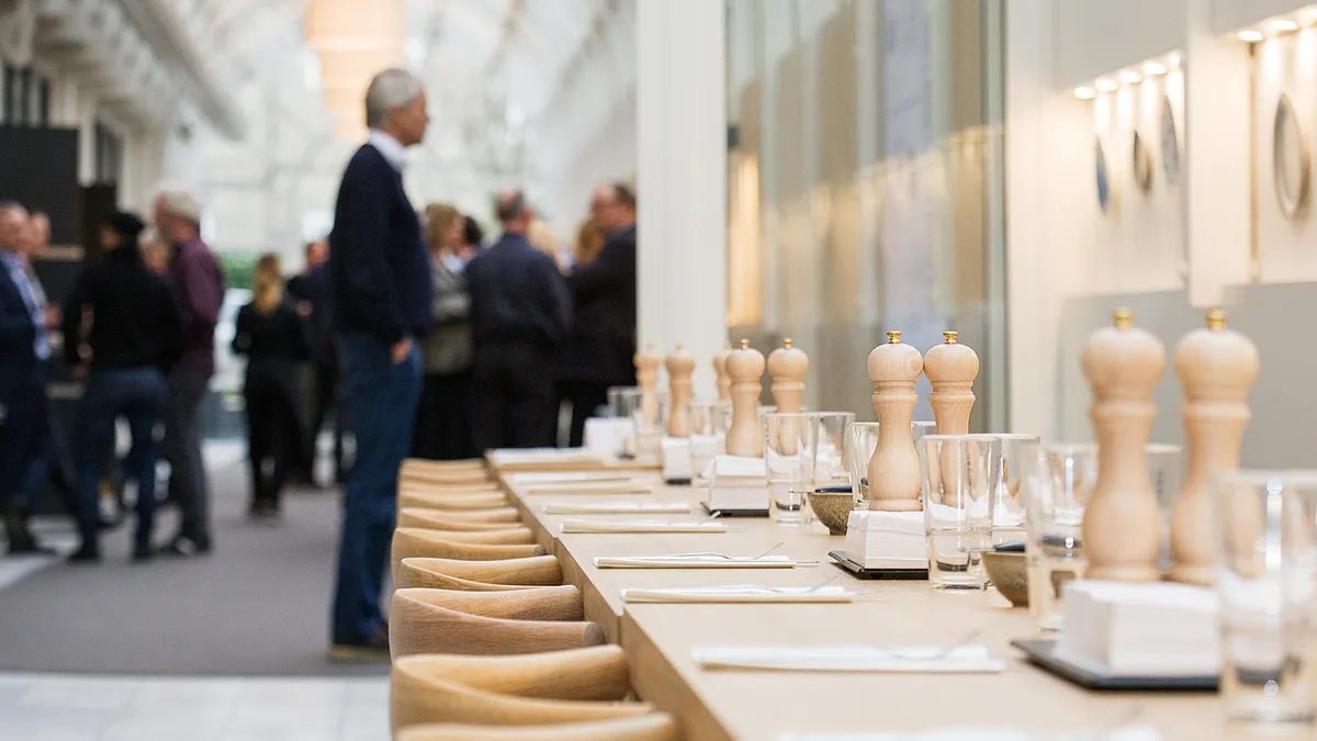 Lyst kontorområde med lyse lofter, borde og stole samt salt- og peberkar. Væggen har lyse lysekroner og et spejl.