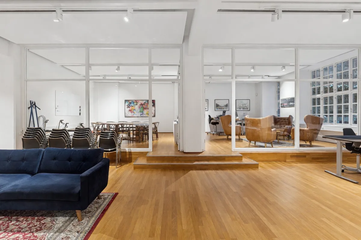 Lyst og moderne kontorrum med lyse lofter og smukke trægulve. En komfortabel sofa og lyse vinduer med udsigt til gaden. Moderne kontormøbler og kunstværker på væggene.