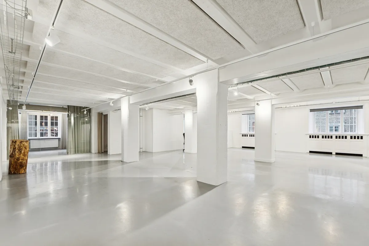 Moderne og industrielt kontor med hvide vægge og lysekroner, lysegulve og store vinduer mod gaden, samt træstamme og radiatorer i hvide vægge