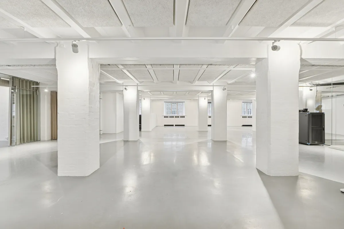 En stor, rummelig og hvid stue med lyse lofter, søjler og ren gulvoverflade samt moderne lysinstallationer. Et stort glasvindue og slanke hvide søjler giver et industrielt og minimalistisk udseende.