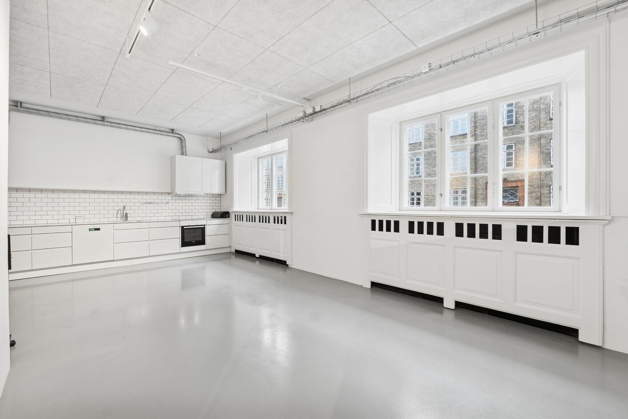 Kontorrum med hvidt loft og vægge, møbler og udstykning i hvidt, store vinduer og køkken med hvide fliser og integrerede apparater