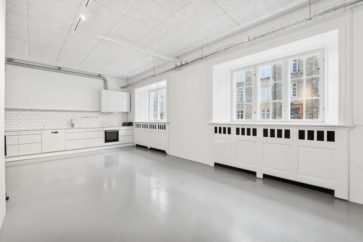 Kontorrum med hvidt loft og vægge, møbler og udstykning i hvidt, store vinduer og køkken med hvide fliser og integrerede apparater