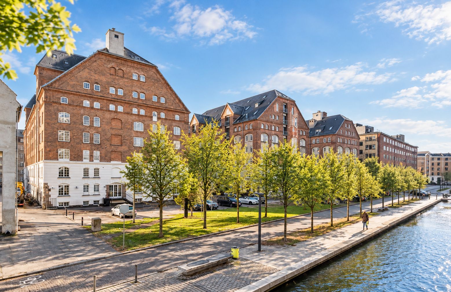 Kontorlejemål med rå og industriel stil på Islands Brygge metrostation, parkerede biler, grønne træer og en person går på en bro langs vandet