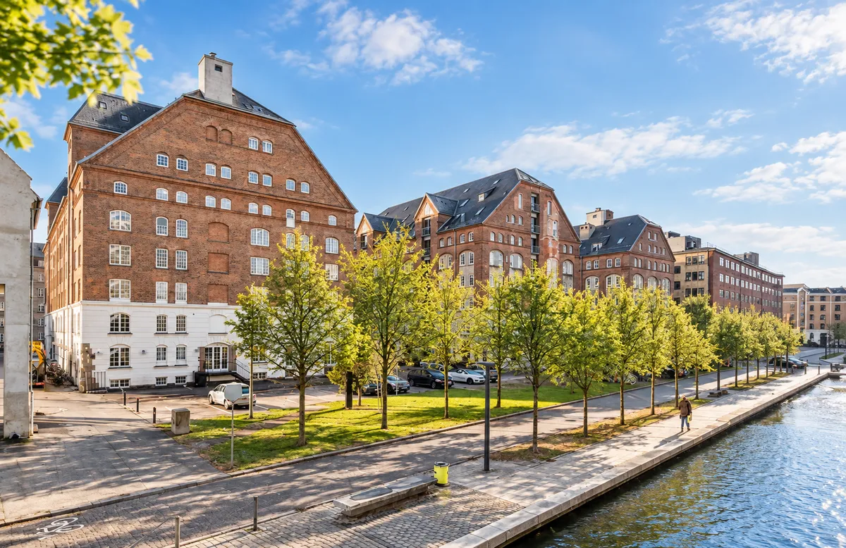 Kontorlejemål med rå og industriel stil på Islands Brygge metrostation, parkerede biler, grønne træer og en person går på en bro langs vandet