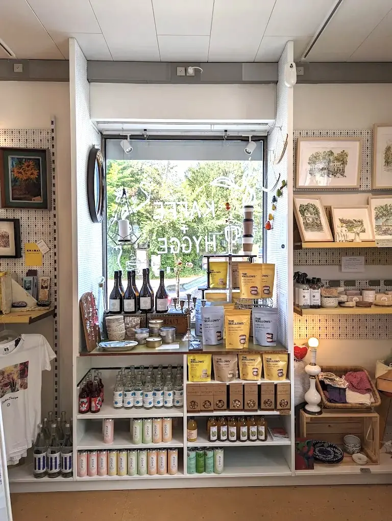 Butik med tøj, kunstværker, snacks, drinks og vin på hylder med udsigt ud ad et vindue med takkekort