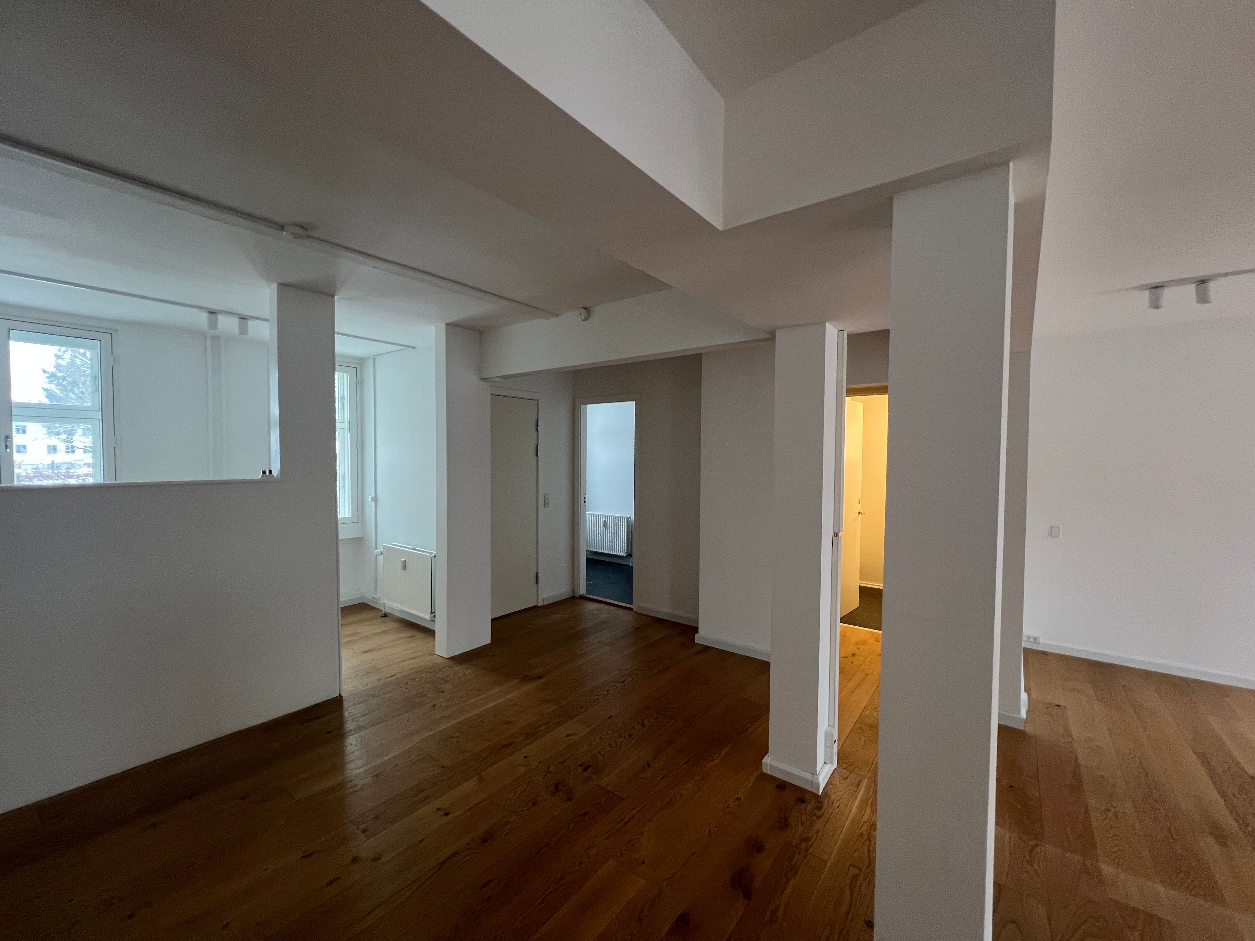 Tom rum med højt til loftet og lyse trægulve, store vinduer og to separate indgange