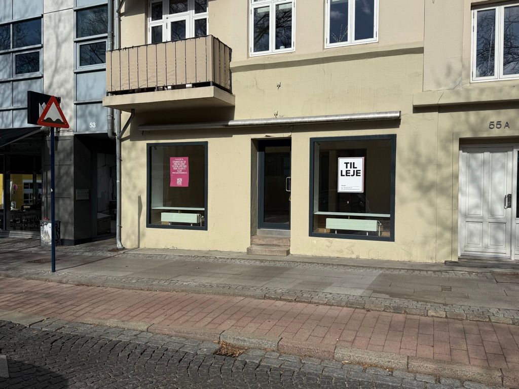 Butik til leje med glasvinduer, nummer 55A på Lyngby Hovedgade i Kongens Lyngby. Vinduerne er lukket, og der er skilte med teksten "TIL LEJE" på vinduet
