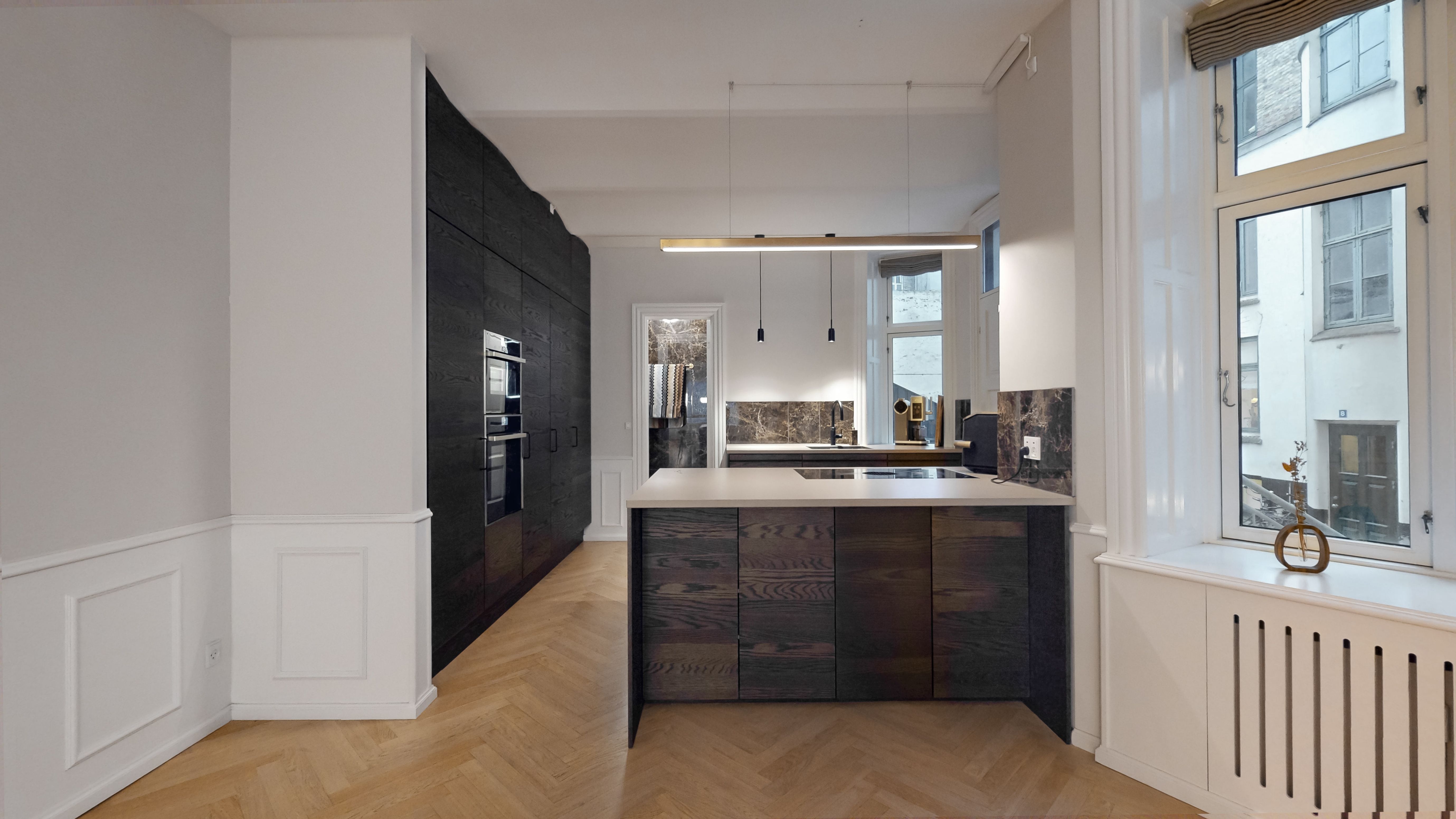 Moderne køkken med massivt træ skabe og marmor loft. Møbler og vægpaneler i hvidt. Køkken med højt gulv og lysekroner. Vindue med udsigt til bygning og lyseruder