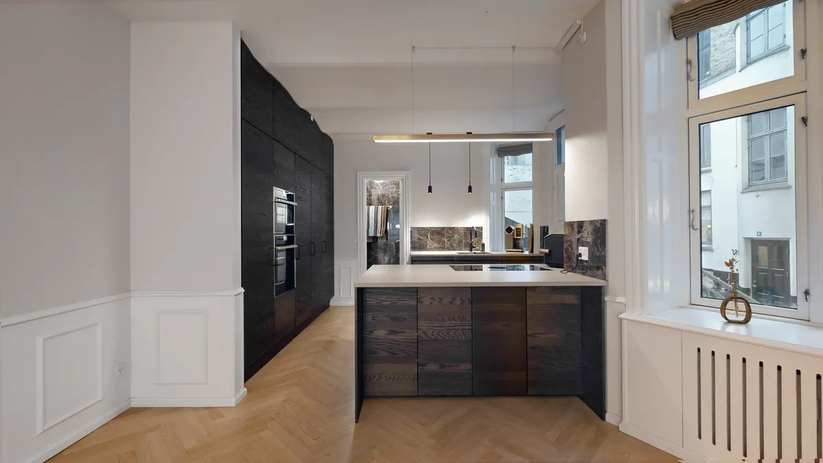 Moderne køkken med massivt træ skabe og marmor loft. Møbler og vægpaneler i hvidt. Køkken med højt gulv og lysekroner. Vindue med udsigt til bygning og lyseruder