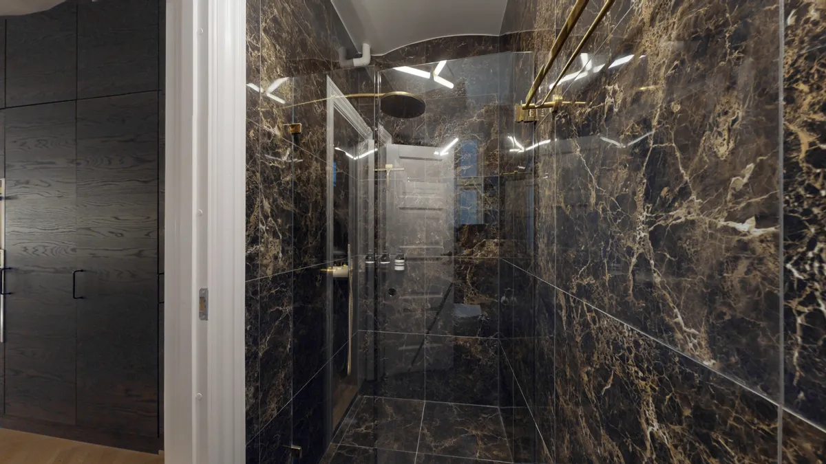 Foto af et moderne badeværelse med marmorbeklædning, guldfarvede håndtaget, og en glashåndbruser med indbygget ventil. Lyse hjørner og elegante designelementer giver rummet et luksuriøst udseende