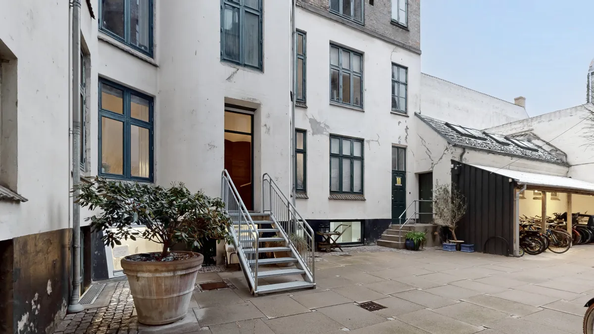 Erhvervsandel med store ruder og terrasse, der vender ud mod en fredelig gade med parkerede cykler og grønne plante potter