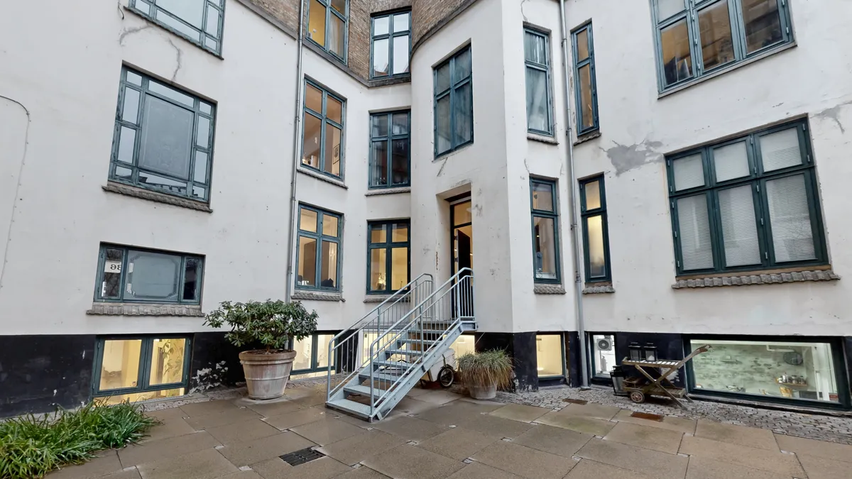 Kort trappeforløb og grønne plantepotter i forgården til erhvervslokaler i København K. Forrude med skrift og nummer 36.