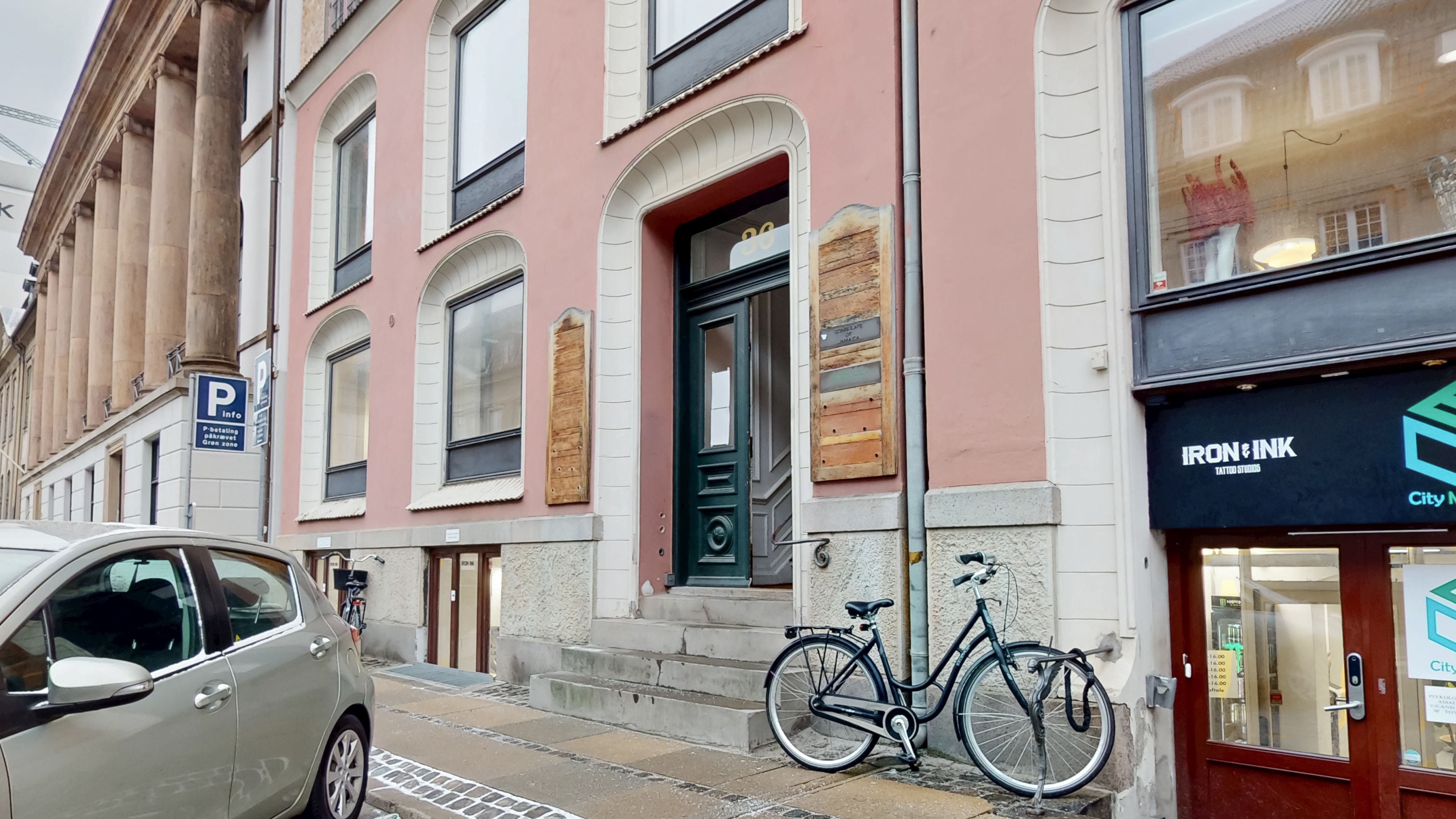 Et parkerede bil og en cykel står foran erhvervslokaler, hvor der står Iron & Ink Tattoo Studios på facaden