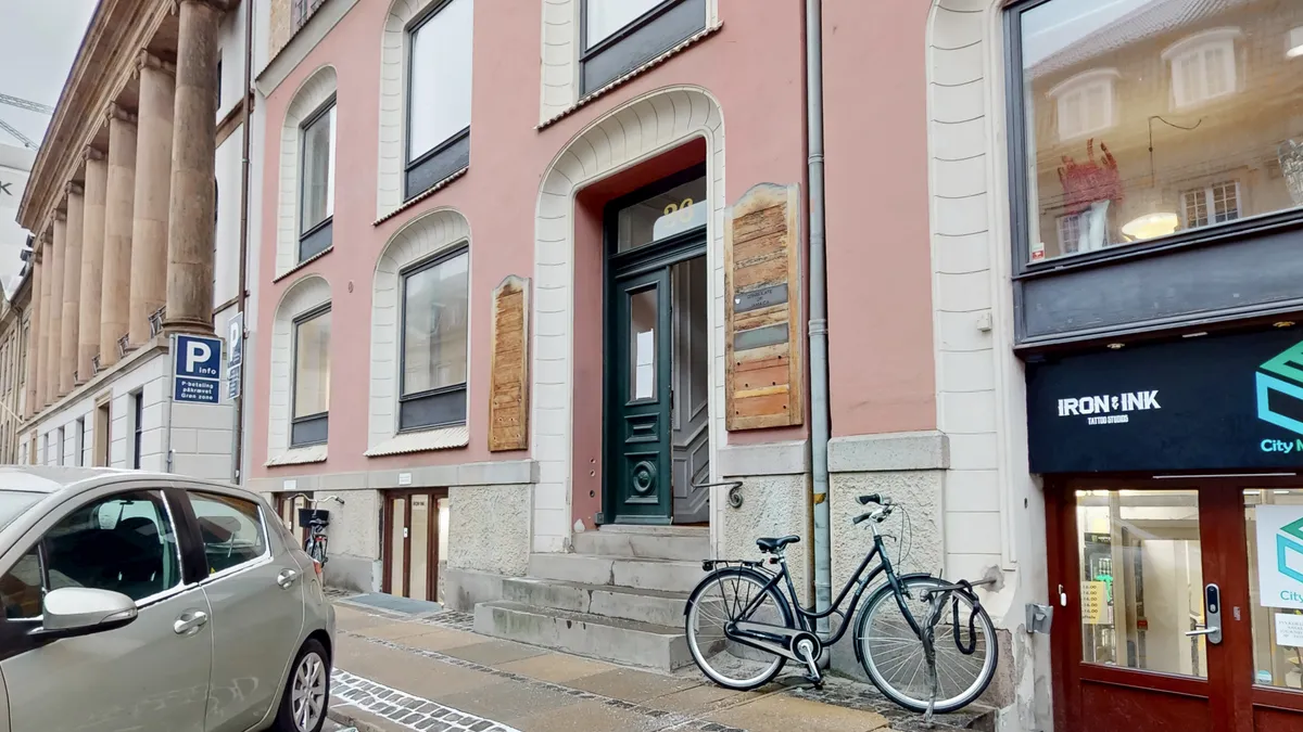 Et parkerede bil og en cykel står foran erhvervslokaler, hvor der står Iron & Ink Tattoo Studios på facaden