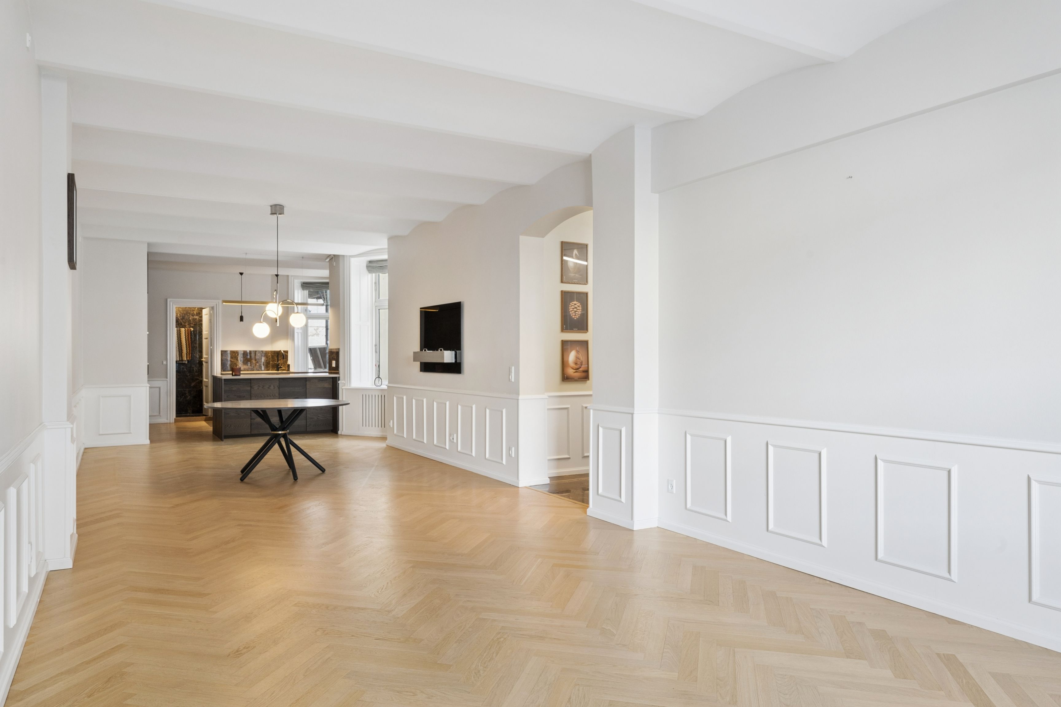 Foto af en tom og pæn stue med højt til loftet, hvide vægge og lyse trægulve, sammen med et elegant bord og en tv-skab i baggrunden