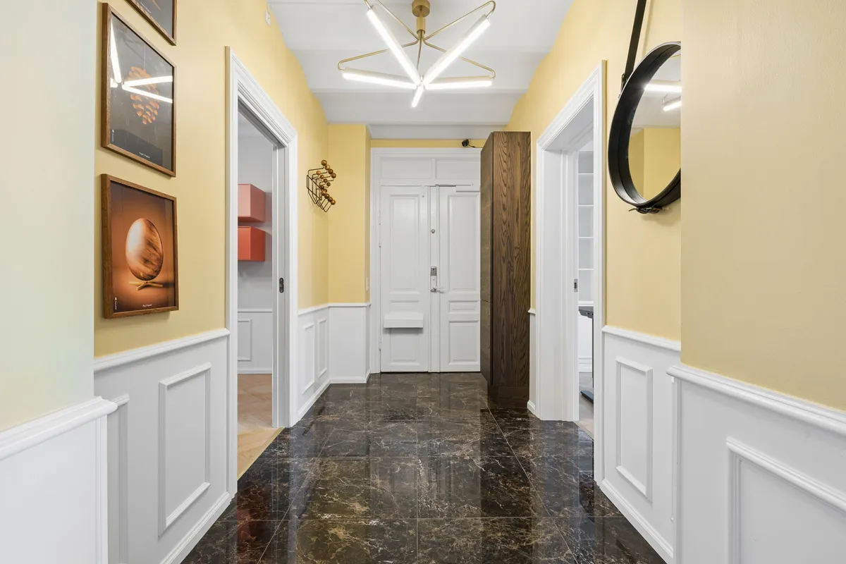 En ren, blank marmorgulv og hvide vægpaneler i en flot indgangshal med lysekronen hængende fra loftet og smukke malerier på væggen