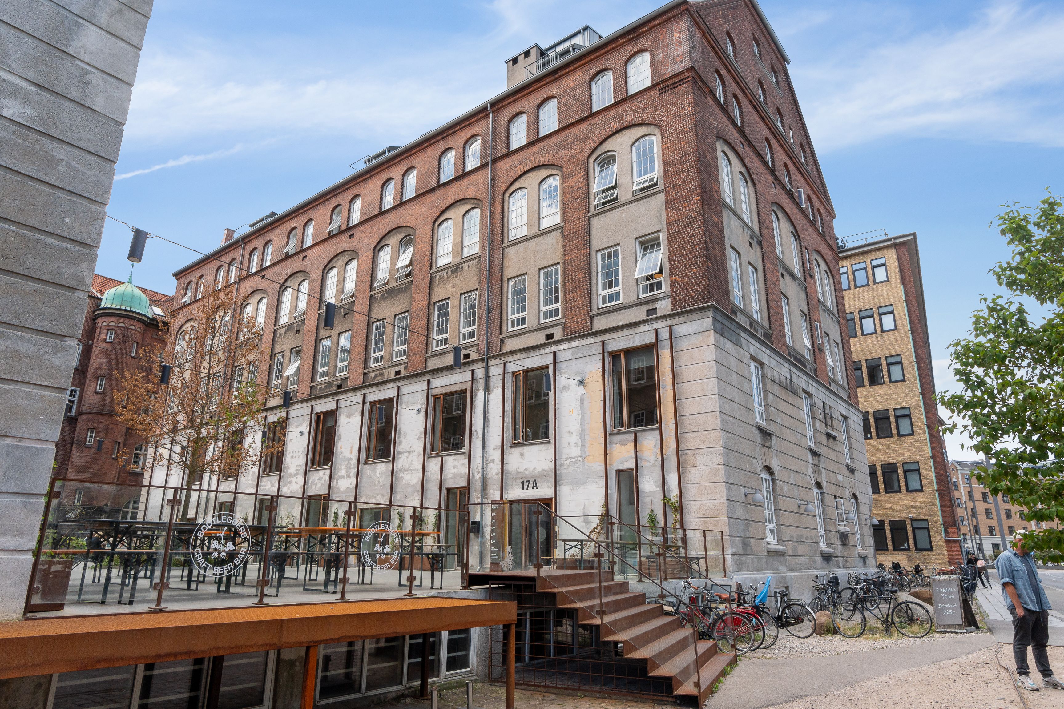Man står udenfor en bygning med flere etager og vinduer, som er tæt ved en vej, hvor der er parkerede cykler