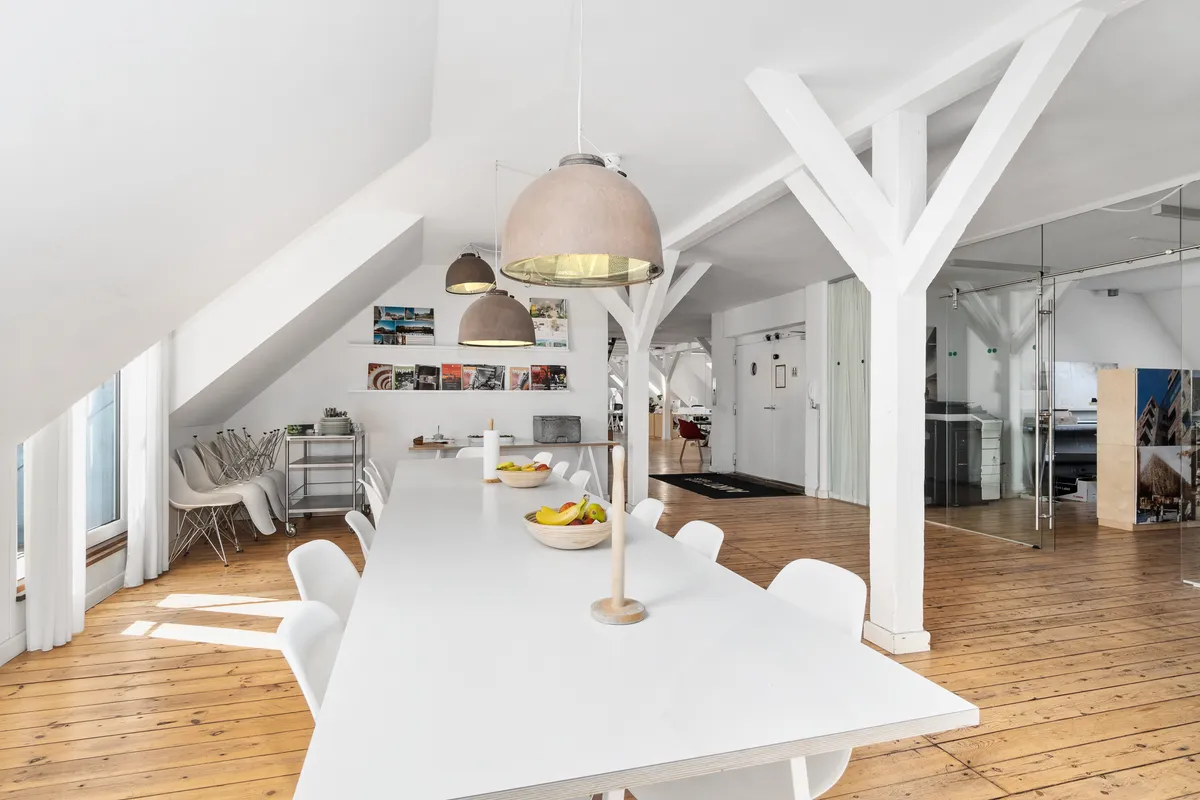Kontorlokaler med højloft og hvidt loft, massivt trægulv og moderne møbler, frugtkurv og lysekroner i loftet