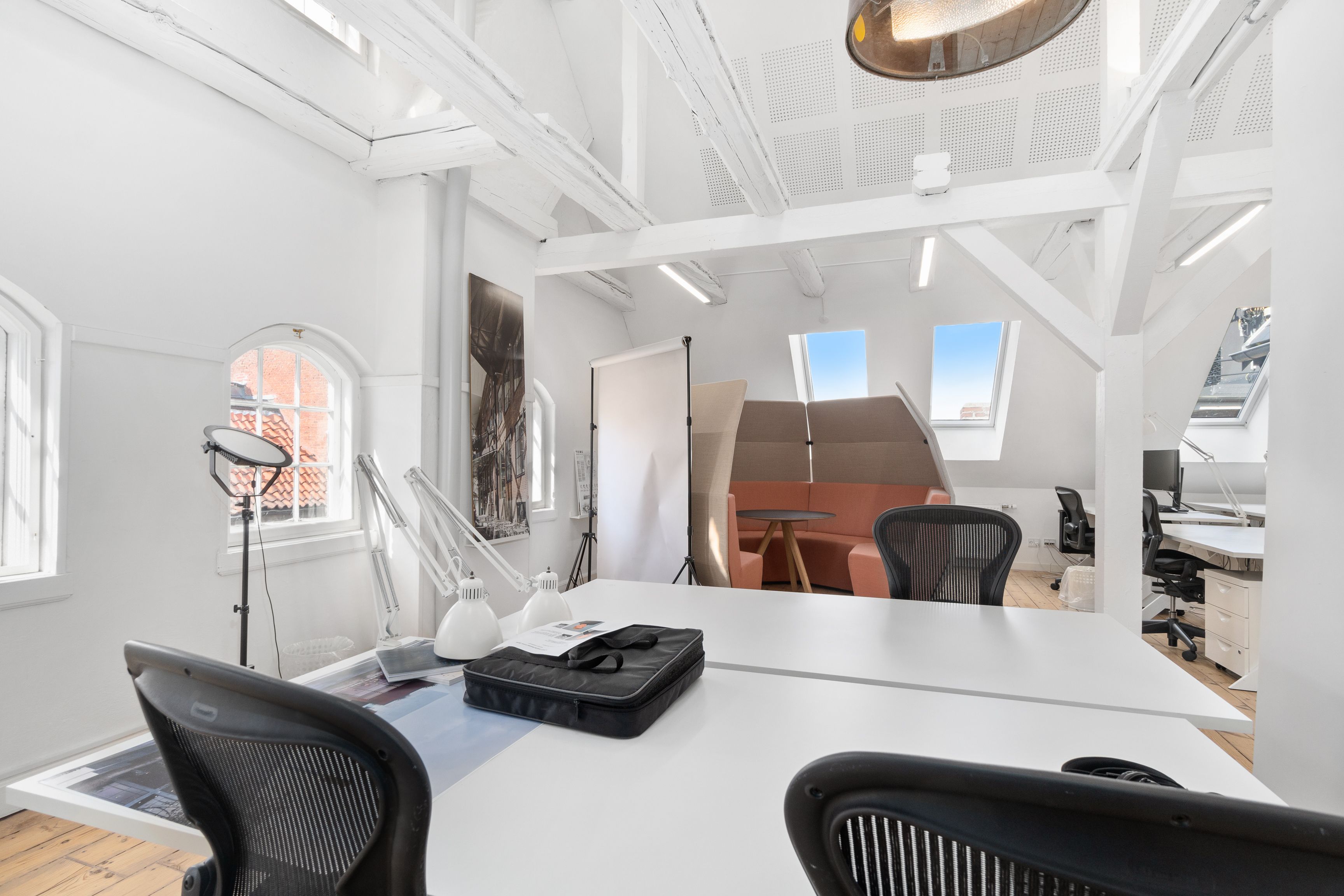 Kontor med højloft, hvidt malet og minimalistisk indretning med lyse loftsvinduer og moderne møbler og teknologi