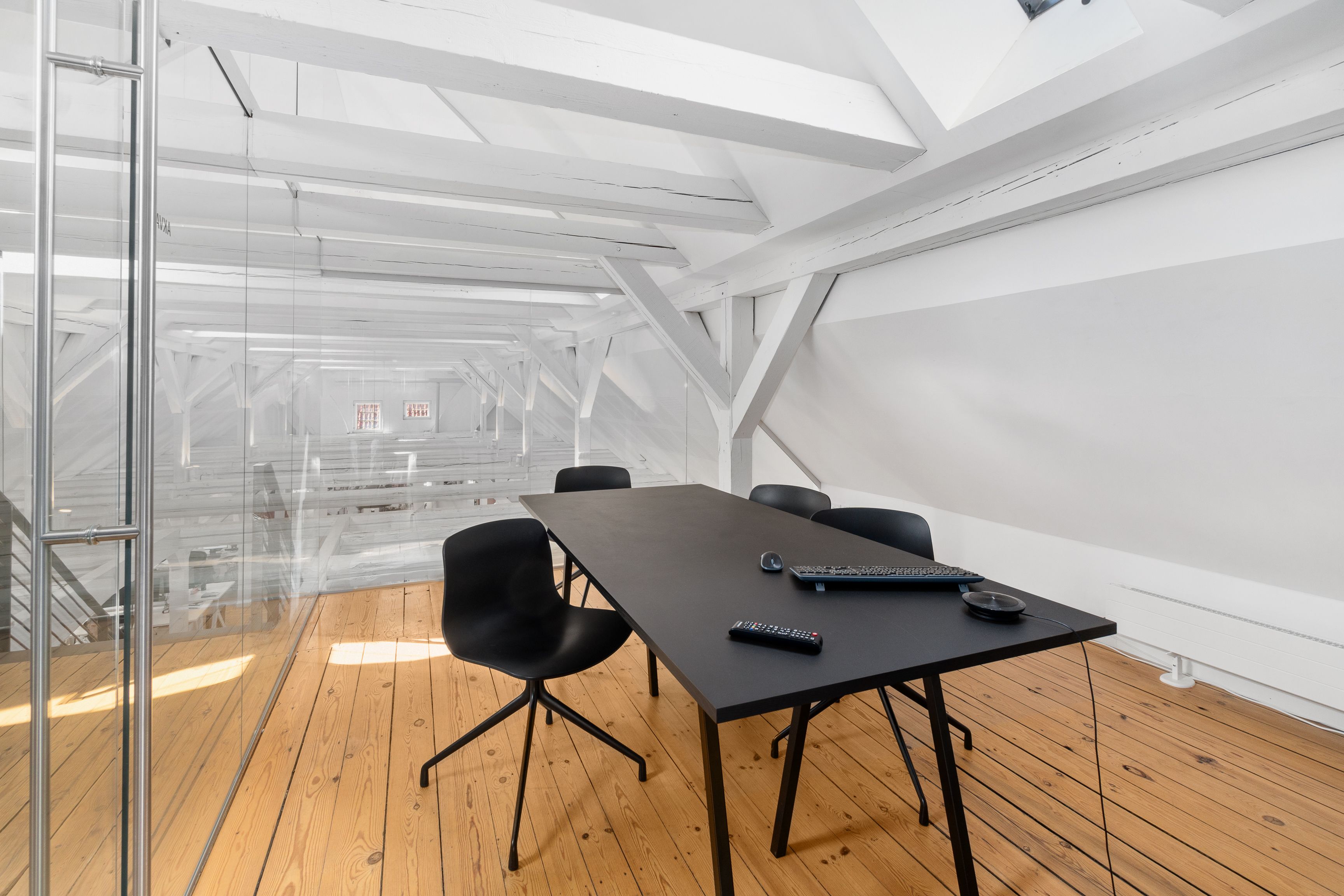 Kontor med sort bord og moderne møbler i loftsrum med hvide bjælker og glasvægge