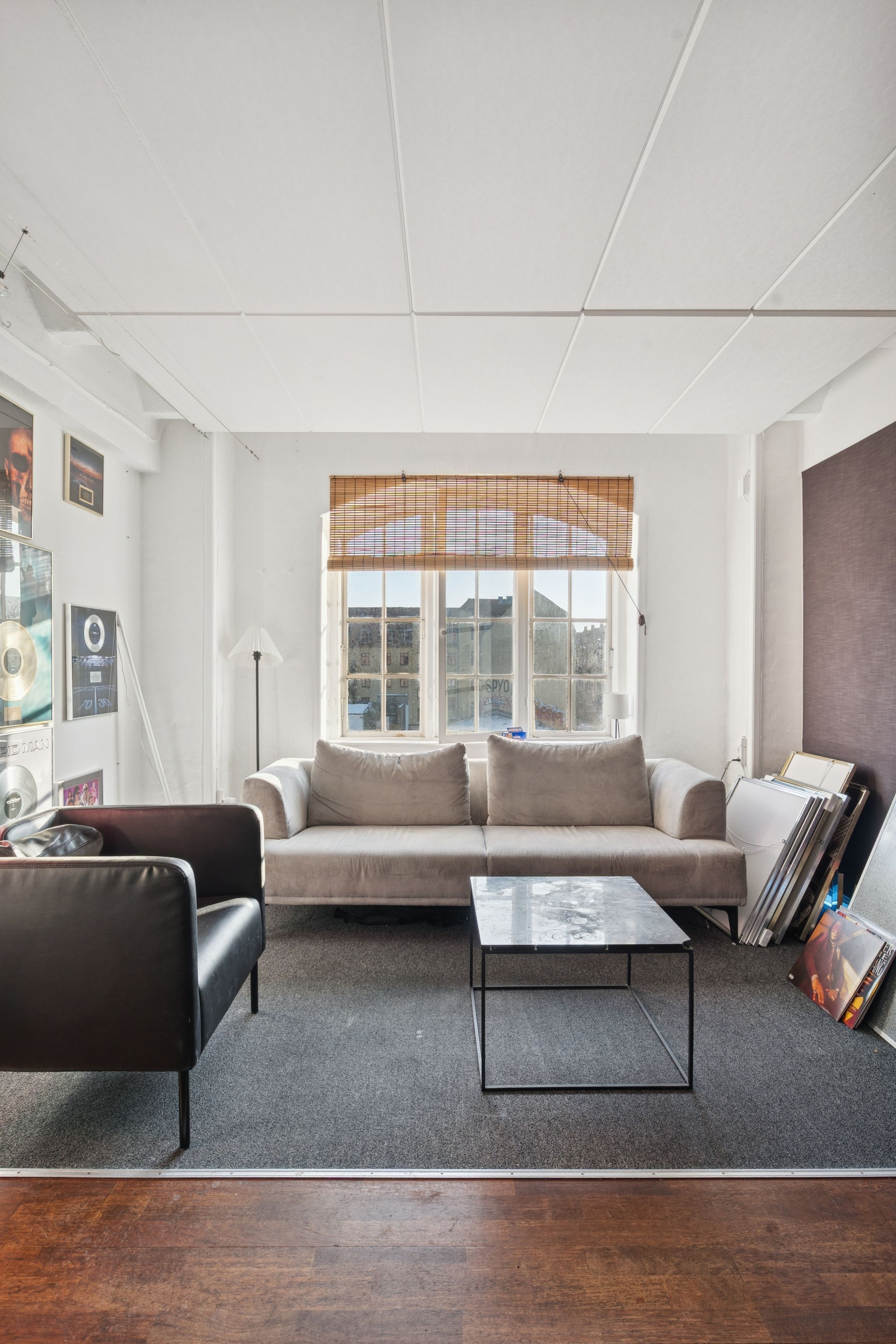 Et rummeligt kontor med højt loft og lysevinduer, hvor en cremefarvet sofa med puter er placeret med et bord og en lampe i midten af rummet