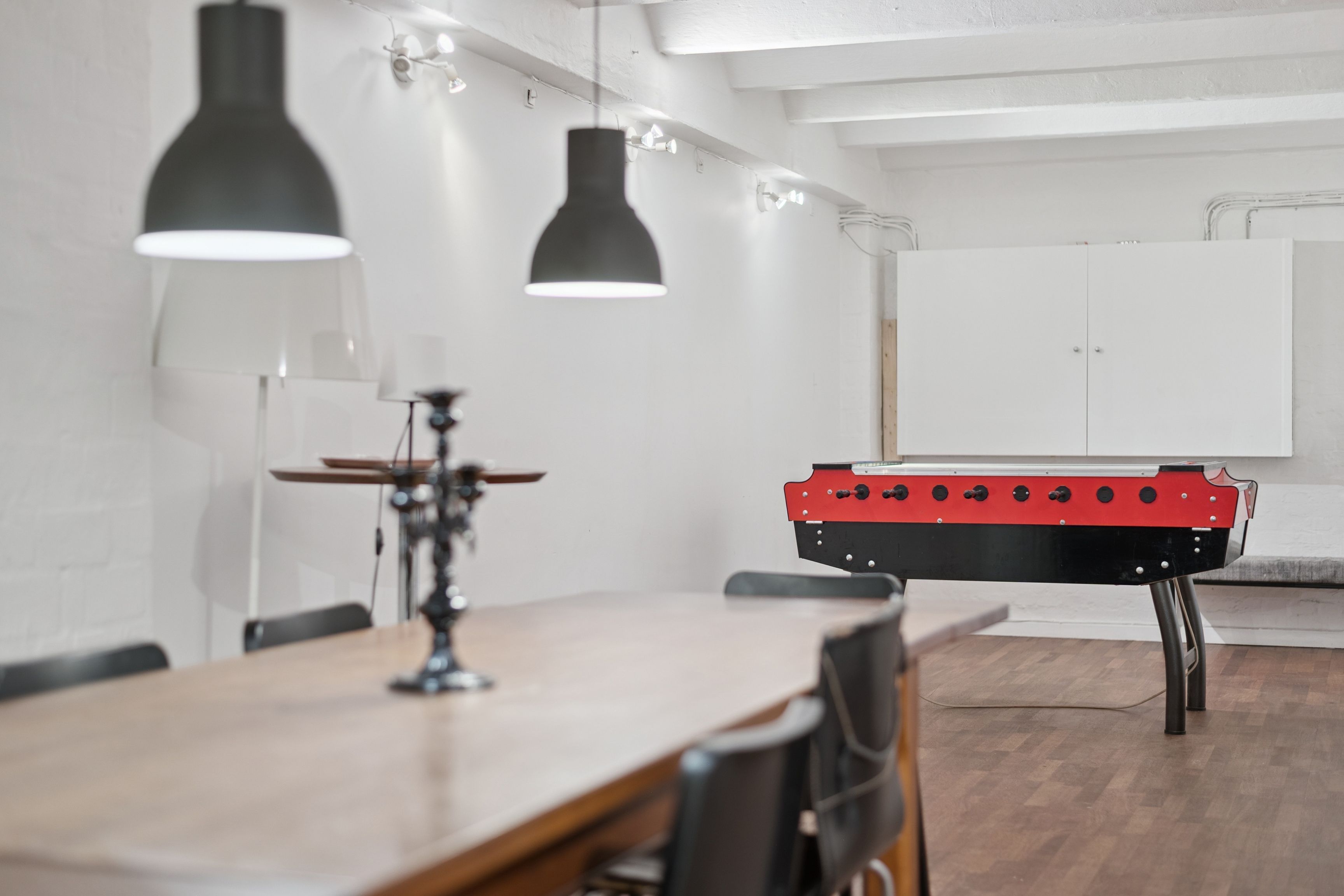 Rummelige kontorlokaler med moderne møbler og en elegant rødt-sort fodboldbord i centrum af lokalet. To loftslys, hvide vægge og trægulv.
