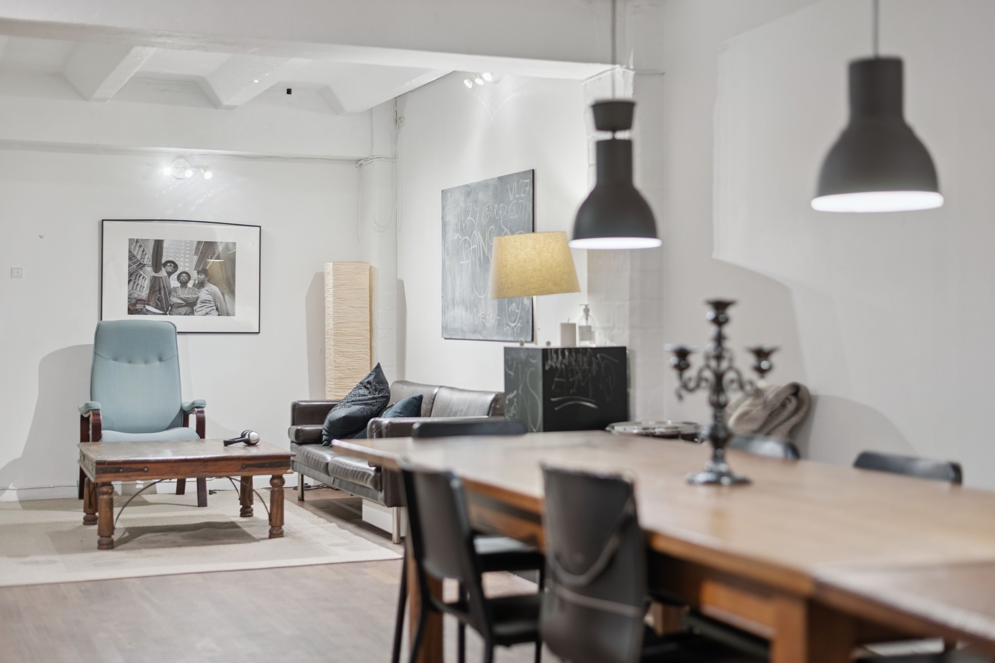 Et lyse loft med lysekroner og en stor spisestue med træbord og stole samt en sovesofa med puder i stuen