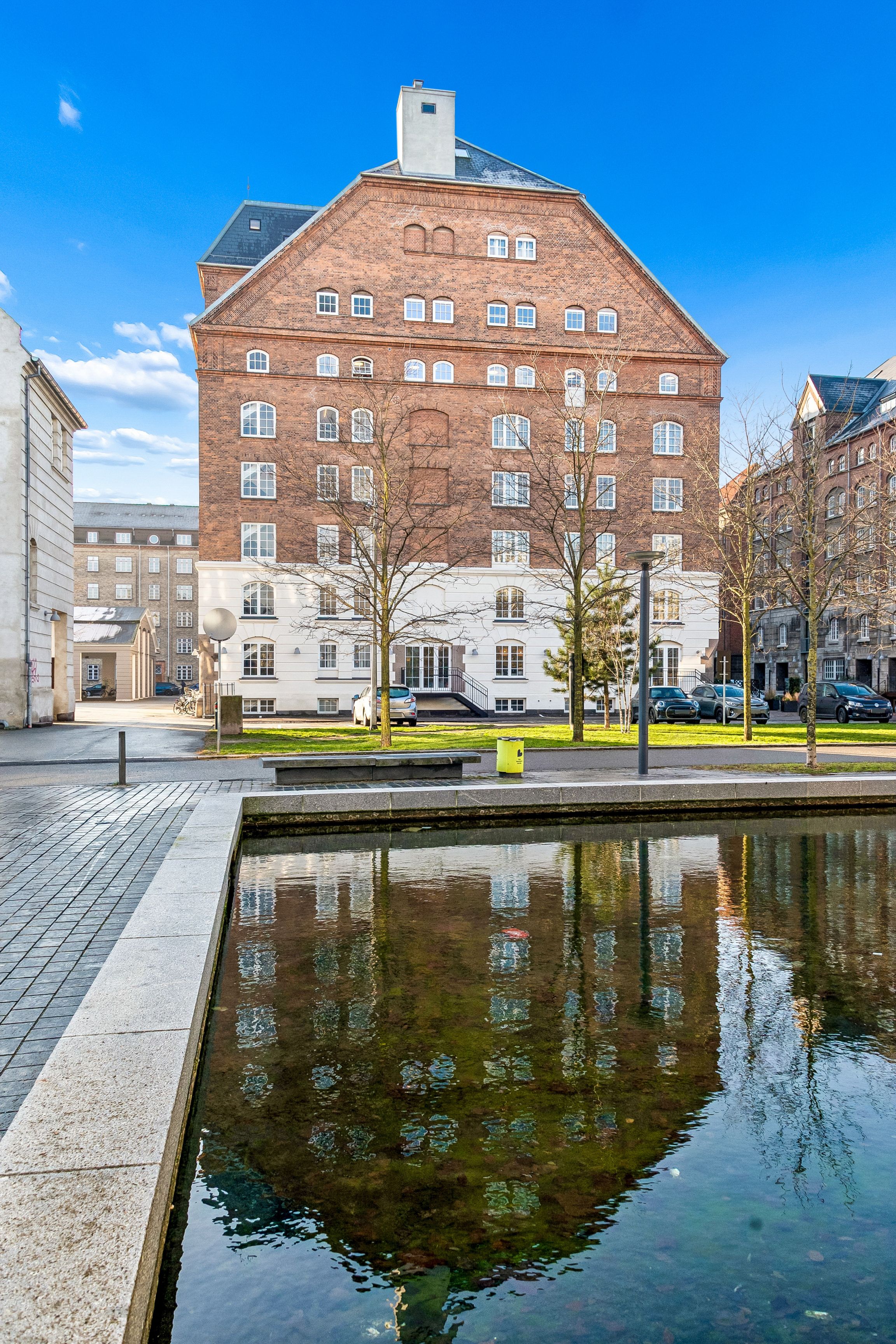 Bygningen med industriel stil ligger ved vandet med smukke refleksioner og en række parkerede biler udenfor. Der er et nytårstræ i vandet og mange vinduer i facaden