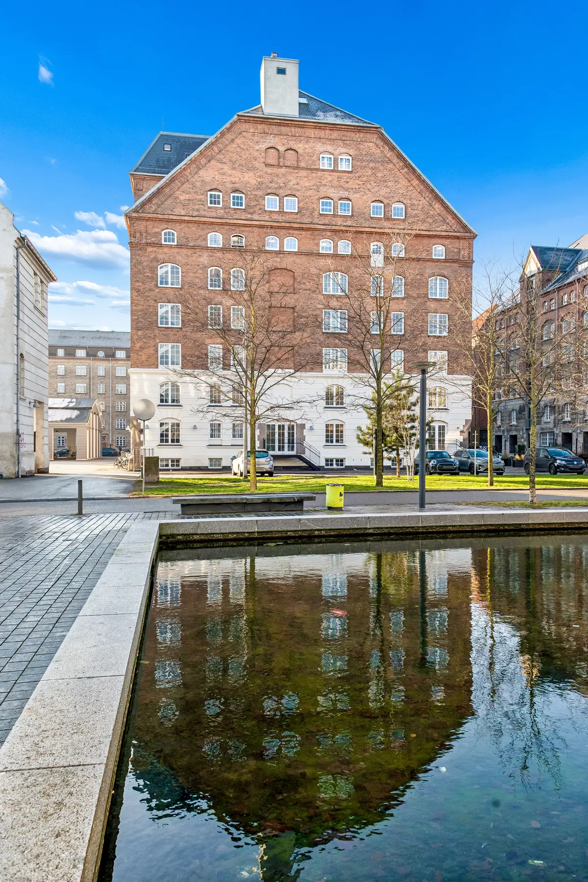 Bygningen med industriel stil ligger ved vandet med smukke refleksioner og en række parkerede biler udenfor. Der er et nytårstræ i vandet og mange vinduer i facaden