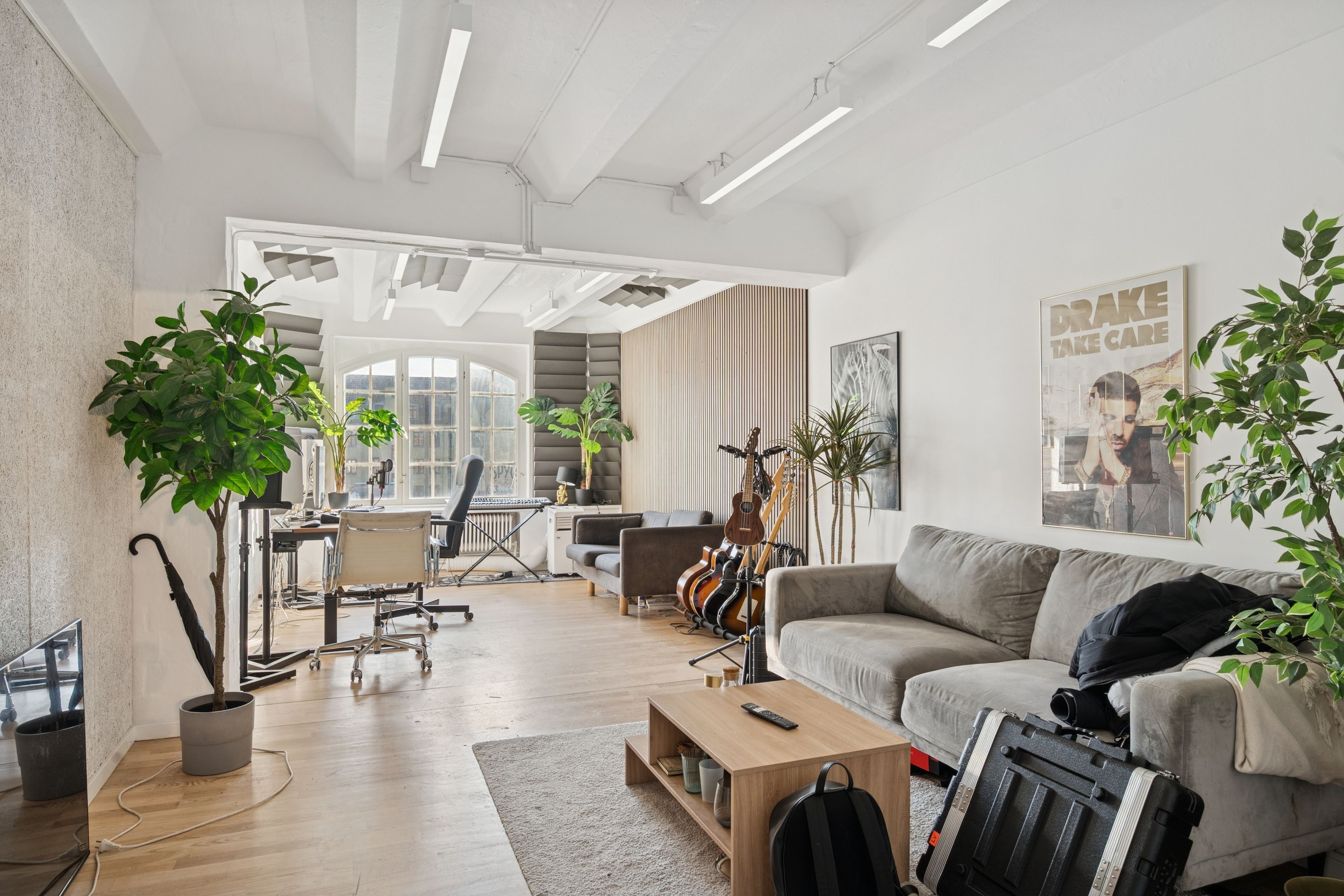 Kontorlejemål med lyse værelser, højloft og industriel stil. Moderne møbler, sofa og skrivebord. Vægge med plante og musikinstrumenter. Indkørsel og vinduer tilbyder masser af naturlys.