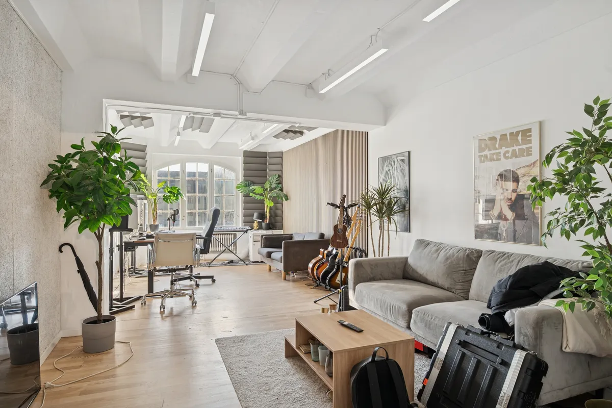 Kontorlejemål med lyse værelser, højloft og industriel stil. Moderne møbler, sofa og skrivebord. Vægge med plante og musikinstrumenter. Indkørsel og vinduer tilbyder masser af naturlys.