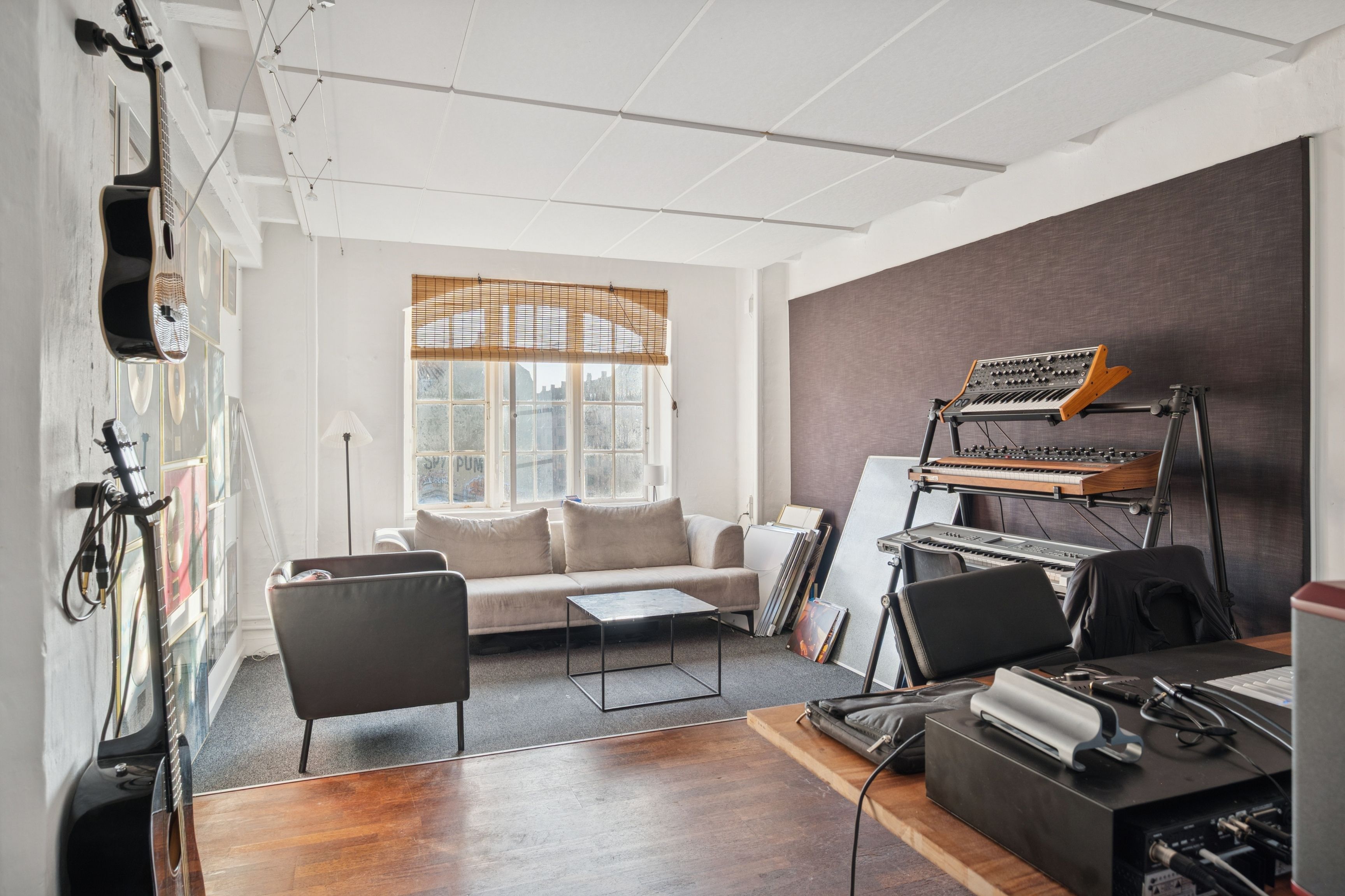 Kontorlejemål med instrumenter, sovesofa, skrivebord, klaver, gulvlampe og vinduer med jalusierne lukket