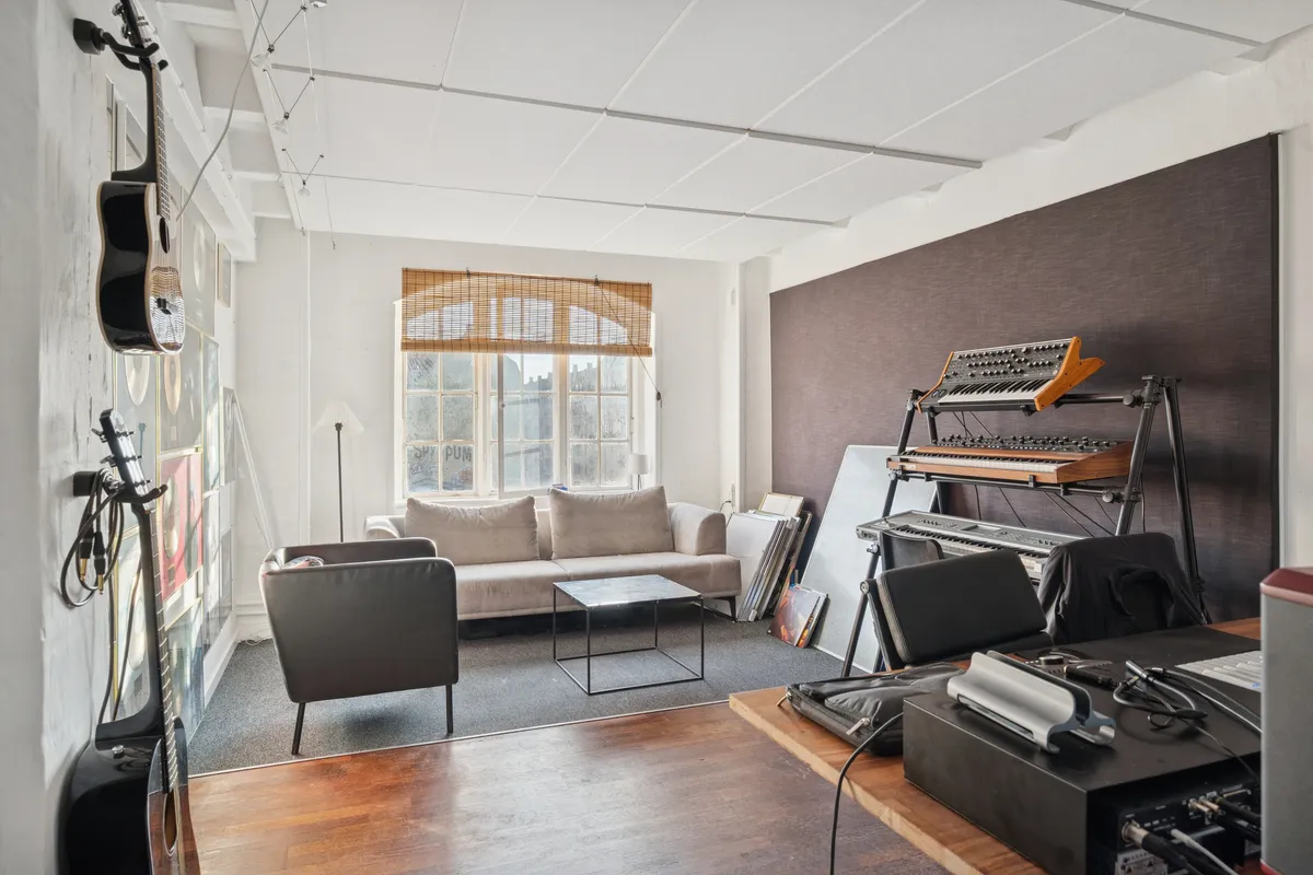 Kontorlejemål med instrumenter, sovesofa, skrivebord, klaver, gulvlampe og vinduer med jalusierne lukket