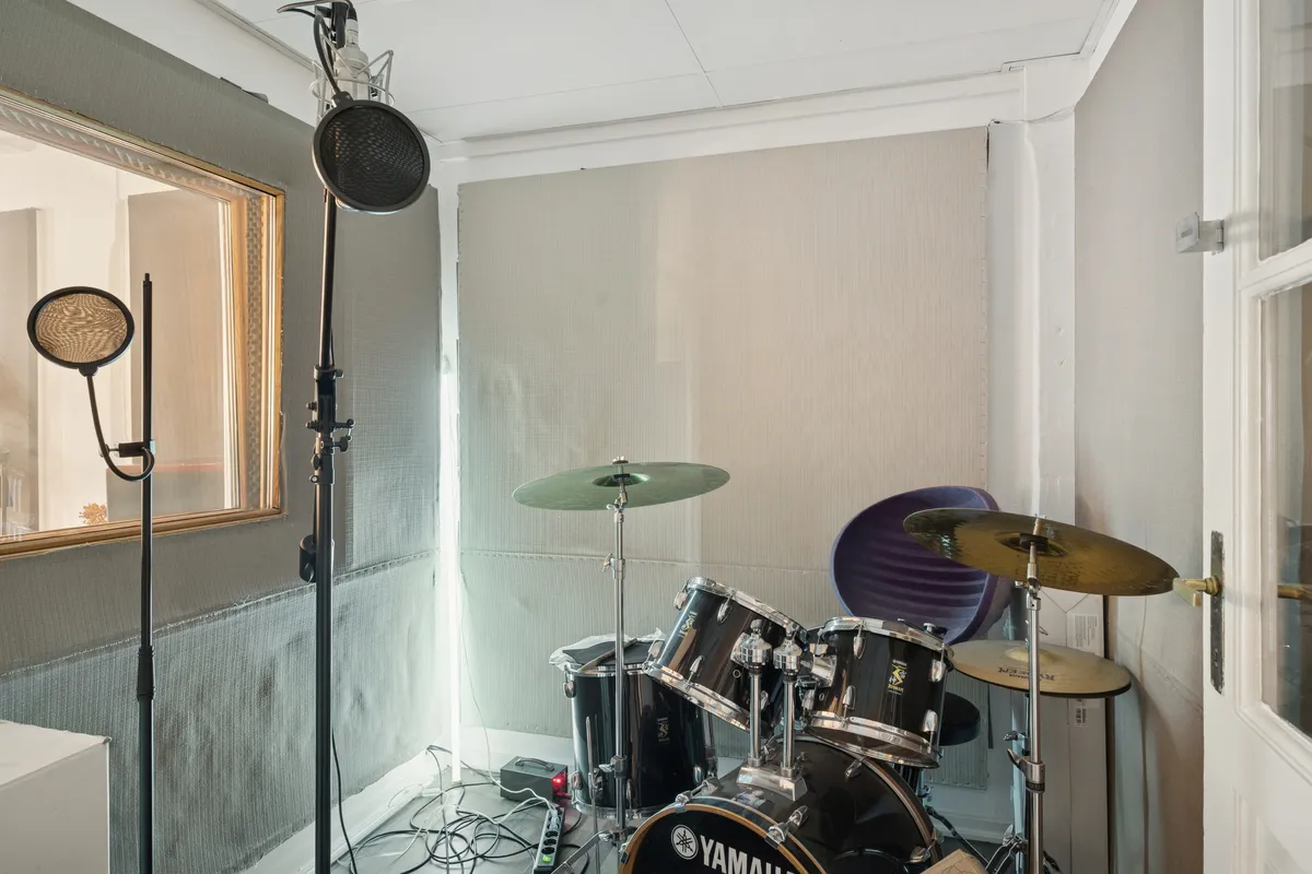 Et lille kontorlokal med Yamaha trommer og mikrofoner til studiooptagelser, samt en gulvmonteret strømforsyning og en glasdør med håndtag