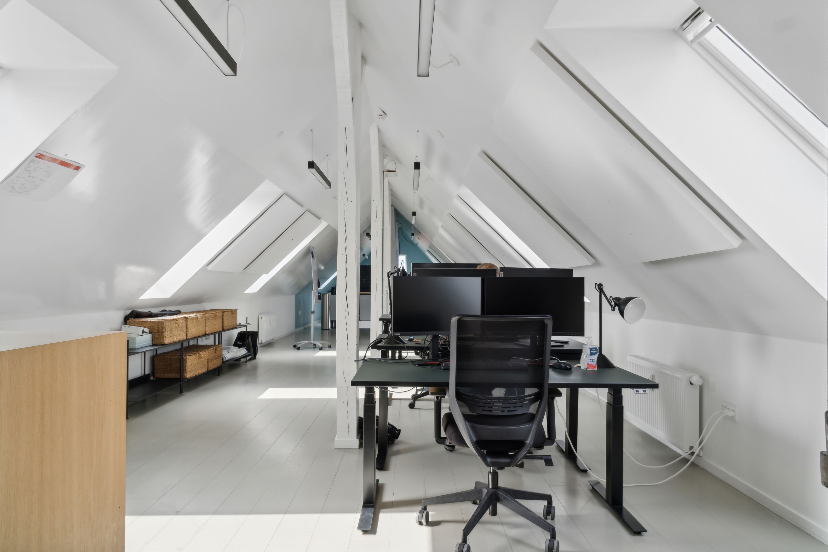 Kontor med lyse lofter og højt til loftet, to monitorer, et skrivebord og en moderne stol i et vellyst lyst rum