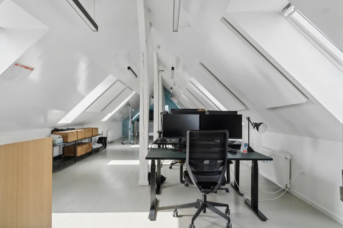 Kontor med lyse lofter og højt til loftet, to monitorer, et skrivebord og en moderne stol i et vellyst lyst rum