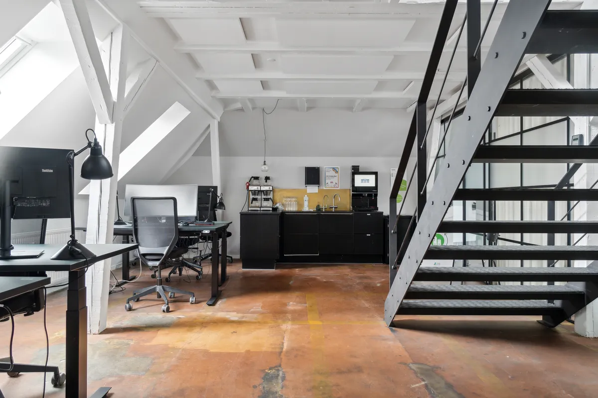 Moderne loftskontor med højloft og højteknologisk udstyr. Minimalistisk design med lysegult lys og lysegul gulvbelægning. Loftskontoret har flere skriveborde, stole og moderne teknologi.