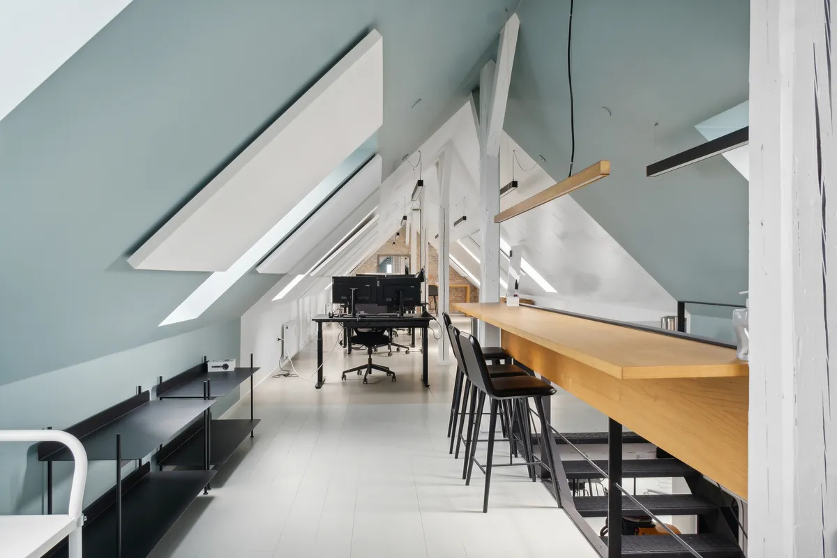 Kontorloft med højloft, loftsvinduer, minimalistisk design, arbejdsborde, lyse loftslampe, lysegule vægge, skråtage, komfortabelt kontor og ideelt til kreative firmaer